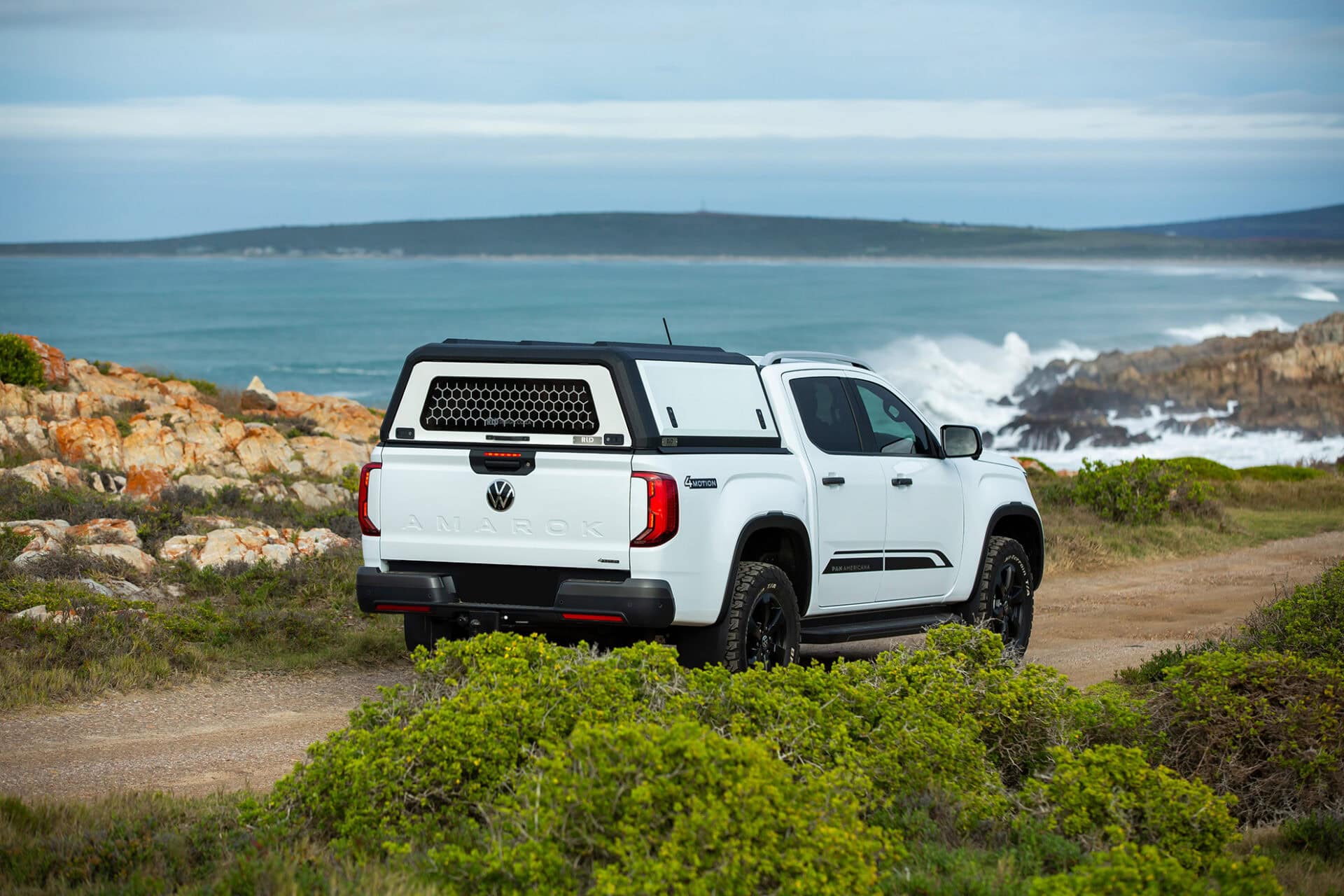 Stainless steel canopy on white pickup truck parked near rocky coastline with ocean view, showcasing durable and stylish vehicular canopy design.