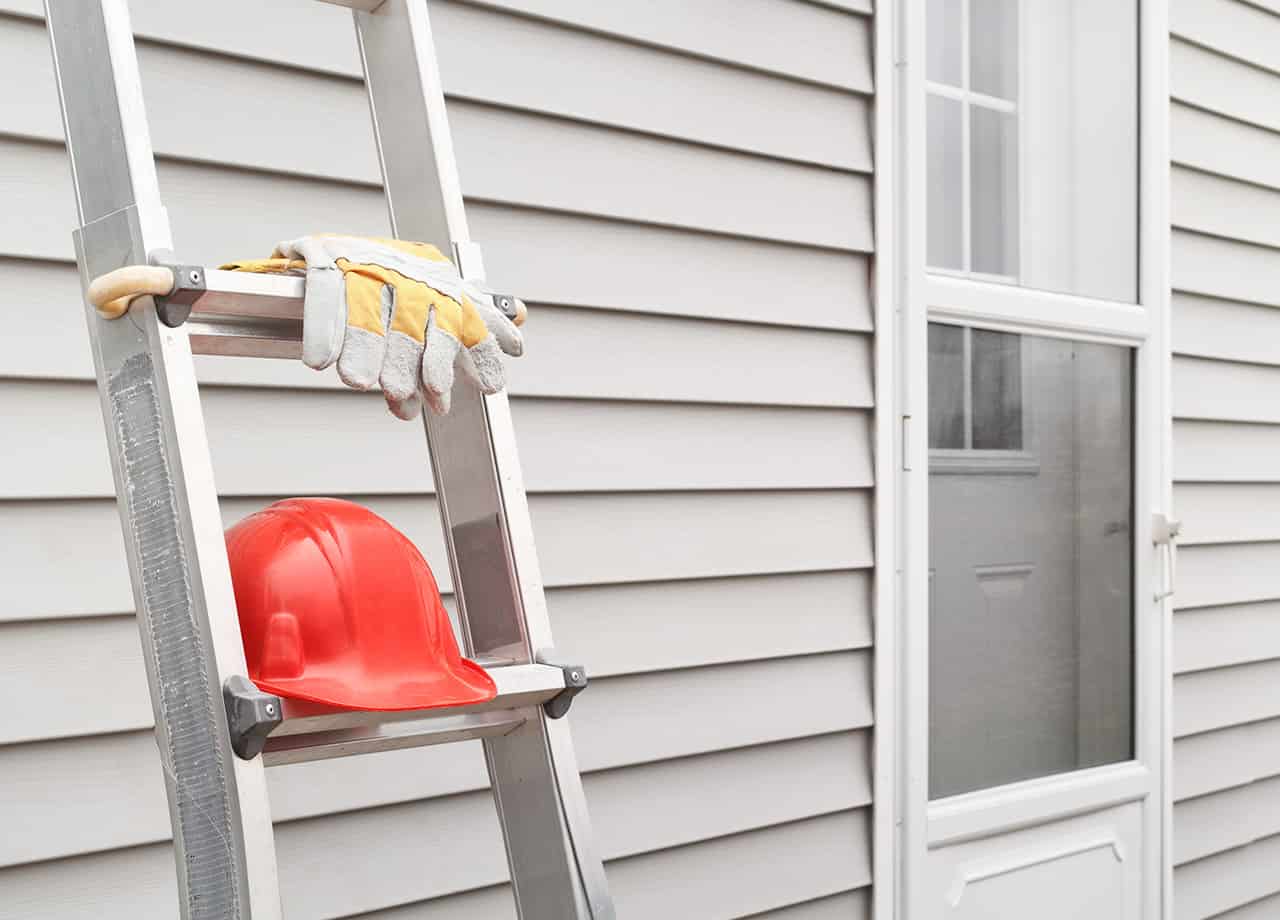 siding repair contractors Milford OH _ Cincinnati OH Image of a ladder leaning against the siding on a home with a hard hat and gloves. Roofing For Troops offers professional siding repairs in Milford OH & Cincinnati OH.