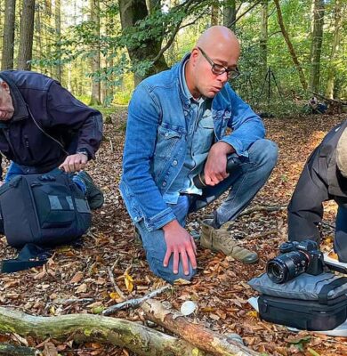 Fotografie van drie mensen die in een bos onderzoek doen naar natuur en biodiversiteit, met professionele uitrusting en camera's voor natuurfotografie en wildlife observation, organisch en natuurlijk achtergrondbeeld.