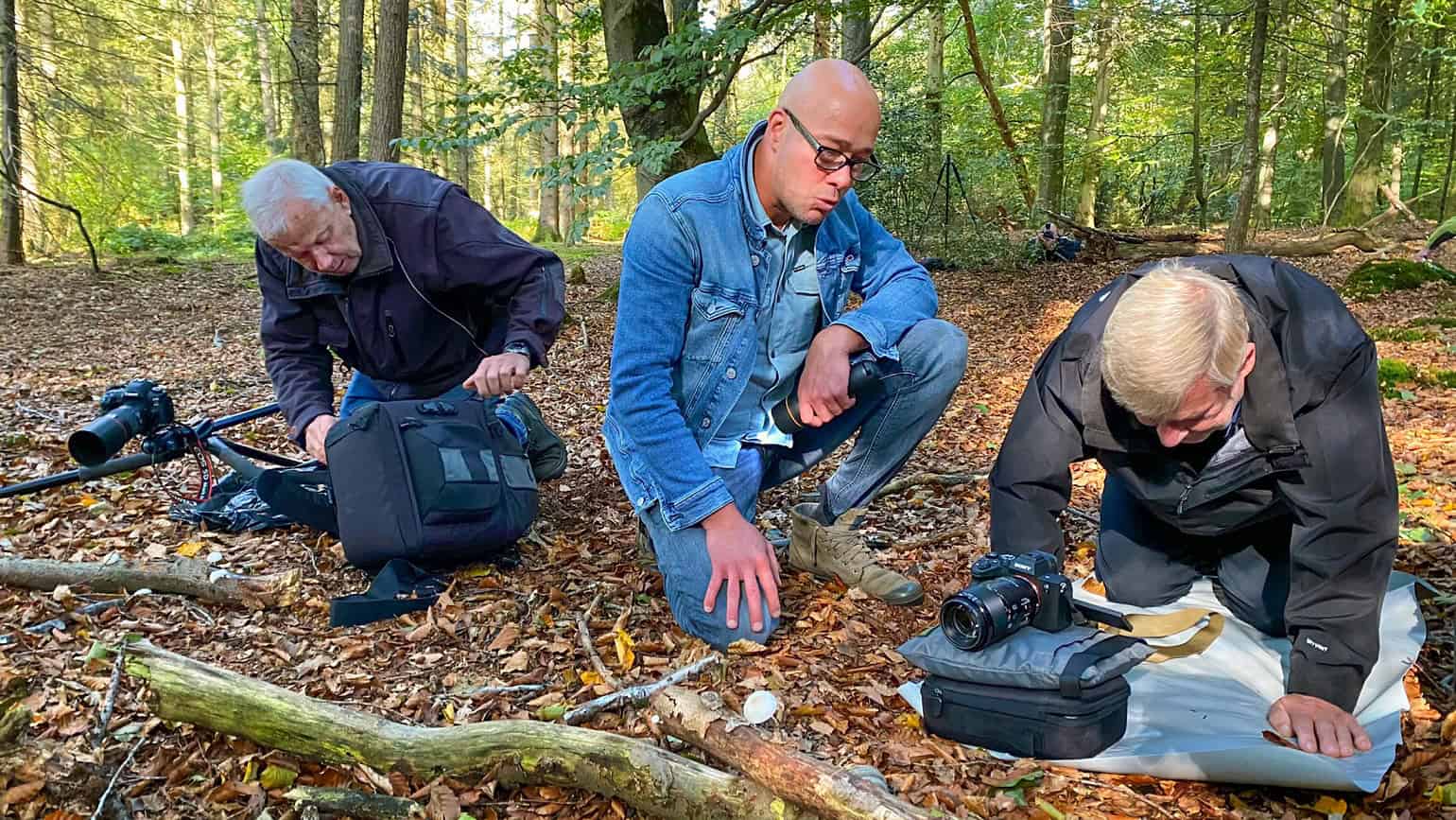 Fotografie van drie mensen die in een bos onderzoek doen naar natuur en biodiversiteit, met professionele uitrusting en camera's voor natuurfotografie en wildlife observation, organisch en natuurlijk achtergrondbeeld.