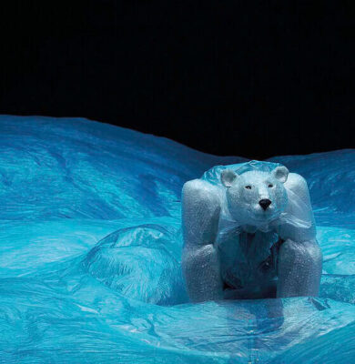 Robuuste ijsbeerfiguur op ijslandschap, gemaakt van kunstmatig ijs en plastic, afgebeeld bij nacht met helder blauw ijs en donkere lucht, symbool voor natuurbescherming en kunstprojecten.