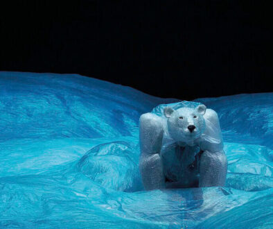 Robuuste ijsbeerfiguur op ijslandschap, gemaakt van kunstmatig ijs en plastic, afgebeeld bij nacht met helder blauw ijs en donkere lucht, symbool voor natuurbescherming en kunstprojecten.