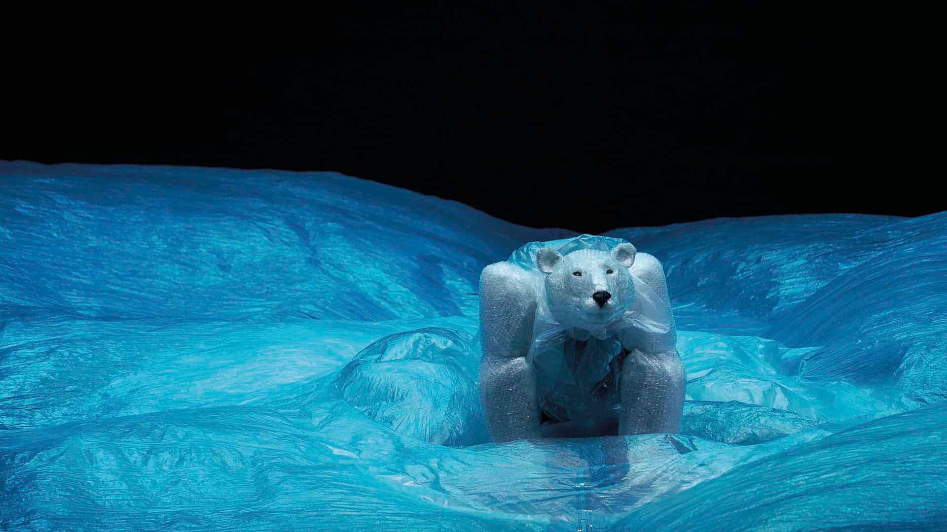 Robuuste ijsbeerfiguur op ijslandschap, gemaakt van kunstmatig ijs en plastic, afgebeeld bij nacht met helder blauw ijs en donkere lucht, symbool voor natuurbescherming en kunstprojecten.