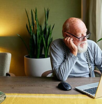 Knusse woonkamer met oudere man workend op laptop, omringd door groene planten, bloemen en sfeervol licht, perfect voor een gezellige en rustgevende sfeer.
