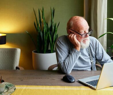 Knusse woonkamer met oudere man workend op laptop, omringd door groene planten, bloemen en sfeervol licht, perfect voor een gezellige en rustgevende sfeer.