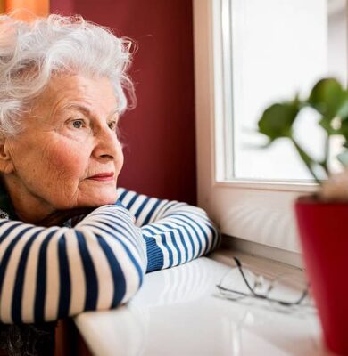 Rustige oudere vrouw kijkt dromerig uit het raam, genietend van het uitzicht, met een groene plant in een rode pot op de tafel voor haar; rust en reflectie. - foto aangeleverd