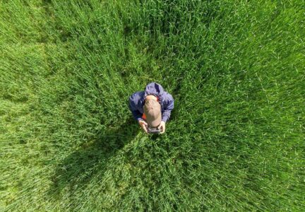 Drone beeld van een persoon in een groen veld die met een remote controle een drone bestuurt, illustratie van drone hobby, fotografie en outdoor activiteiten.