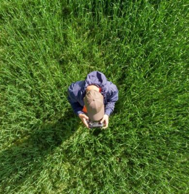 Drone beeld van een persoon in een groen veld die met een remote controle een drone bestuurt, illustratie van drone hobby, fotografie en outdoor activiteiten.