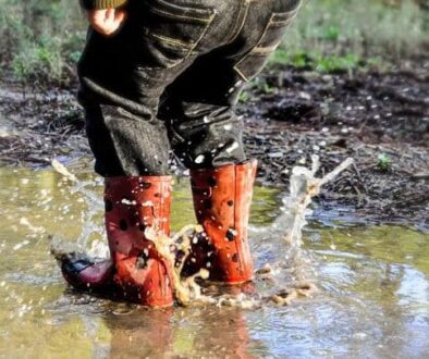 Kind met oranje rubberlaarzen waden door modderig water in een natuurgebied.