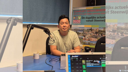 RTV SLOS presentator tijdens interview in radiostudio met RTV SLOS banner op achtergrond.