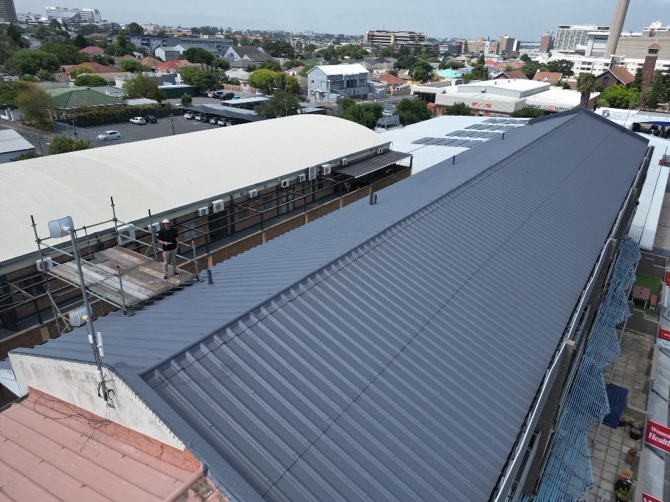 Metal roof with new dark gray coating in an urban commercial area, showcasing durable and weather-resistant rubber roofing solutions.