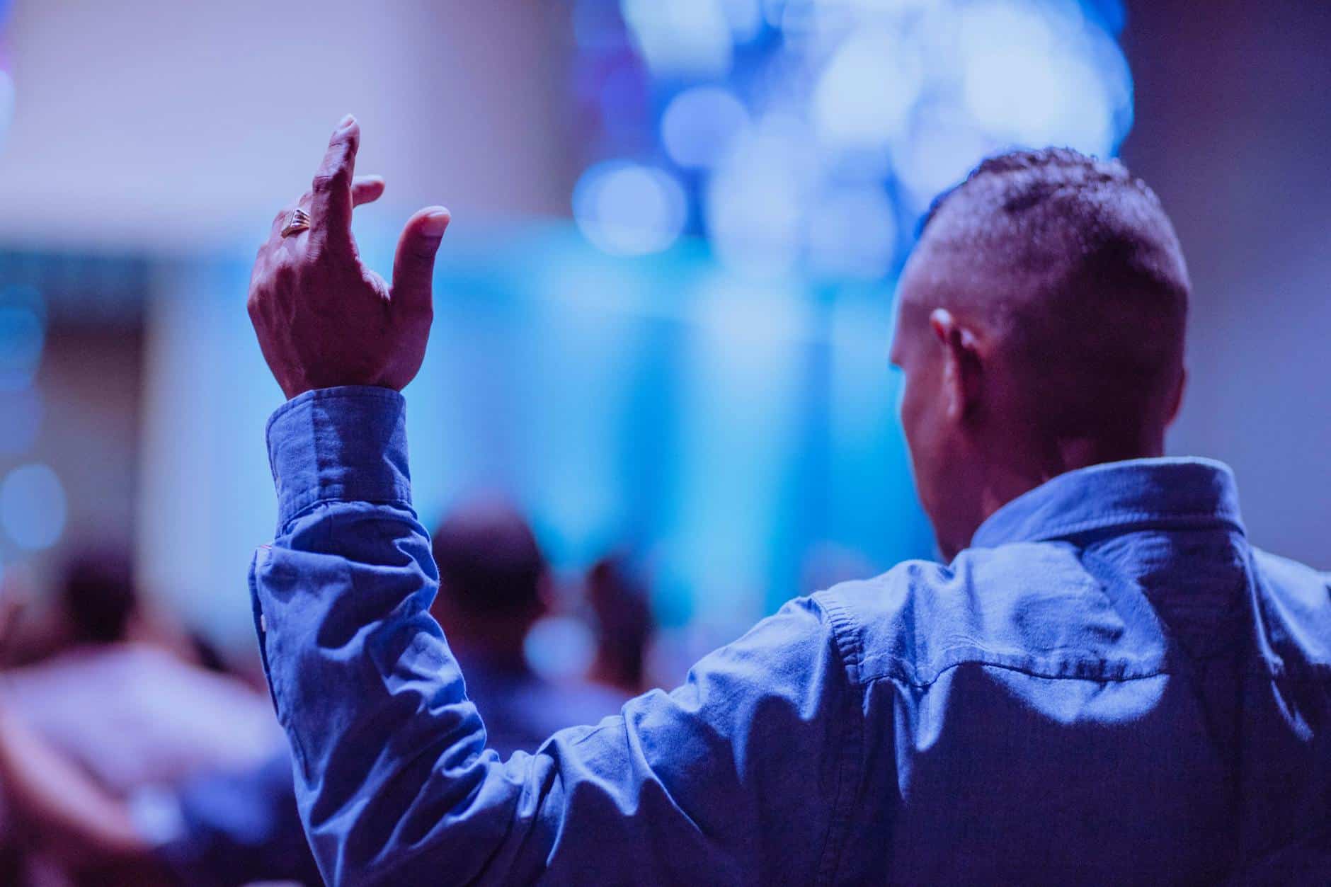 Man raising hand at motivational coaching event, inspiring growth through movement and faith.
