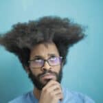 Man with glasses pondering mental health and coaching strategies.