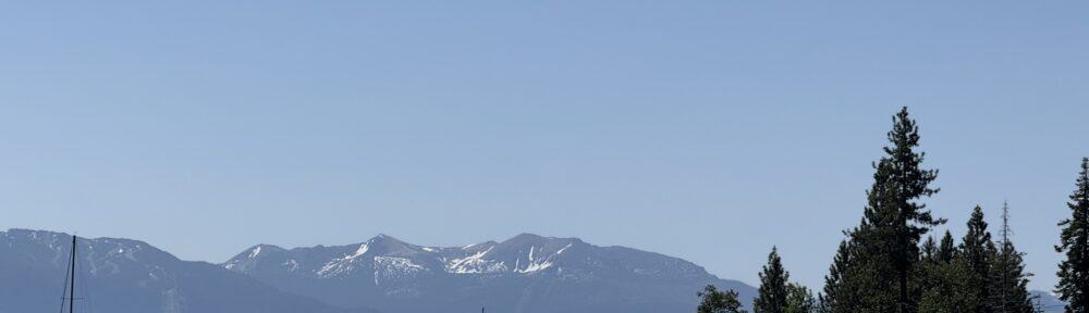 Boats floating on calm lake with mountain backdrop and pine trees, peaceful summer scenery for outdoor recreation and water sports.