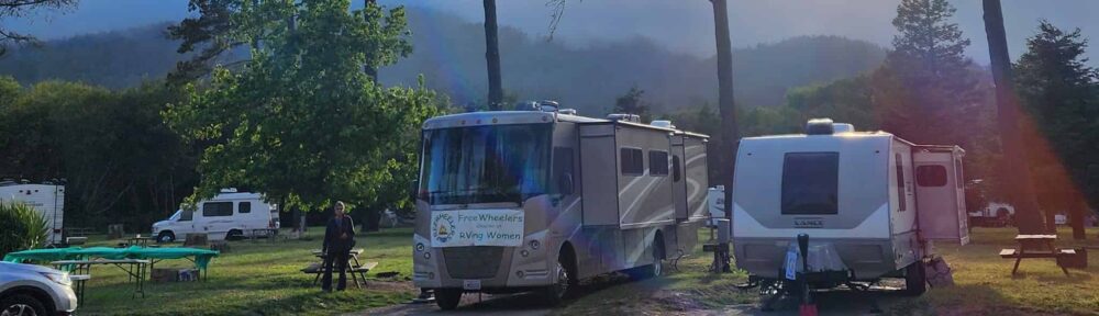Relaxing outdoor scene with RVs and campers at a forested park during sunrise, highlighting the FreeWheelers RVing group enjoying nature and community.