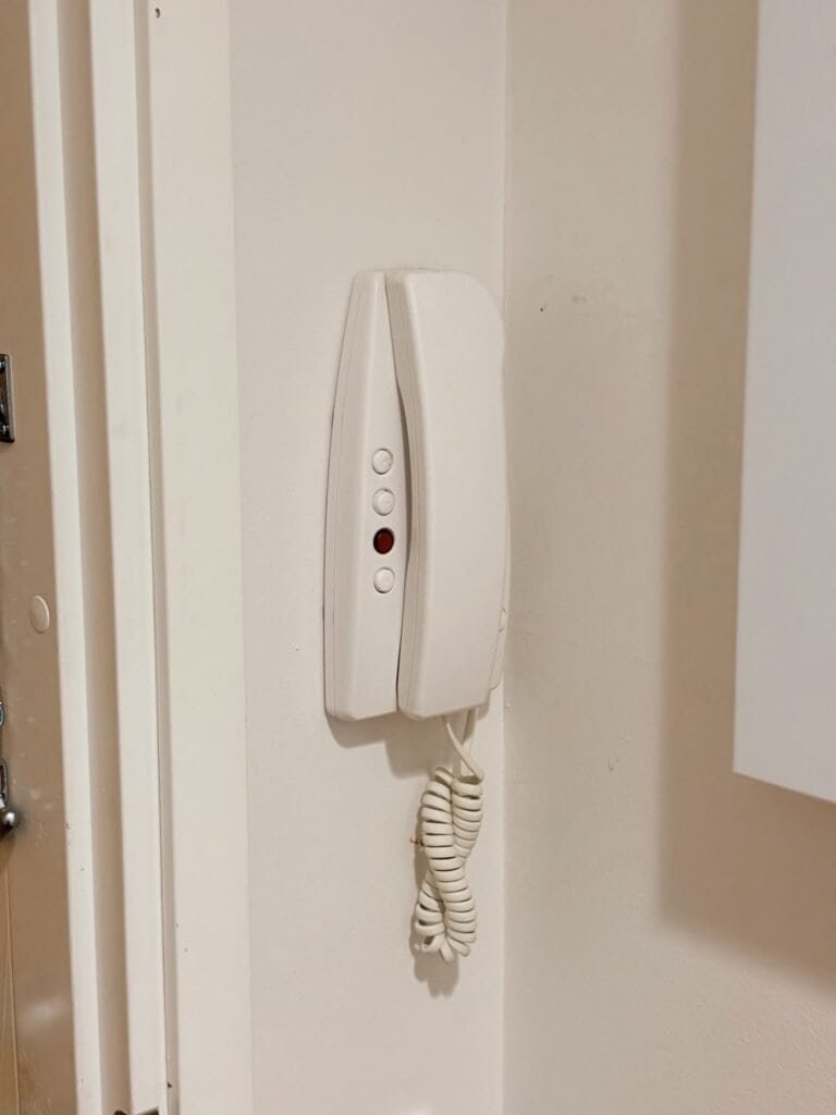 Sähköpuhelin asennettuna sisäseiniin, valkoinen väri.