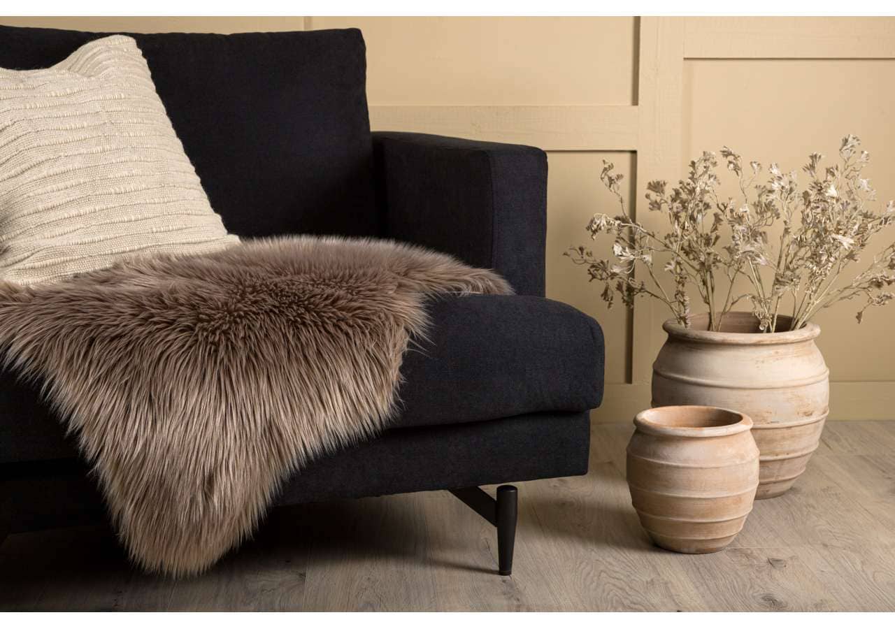 Mjukt fårskinn på svart soffdyna, stilfull inredning, beige växtkrukor, Skandinavisk design, Sängfabriken.