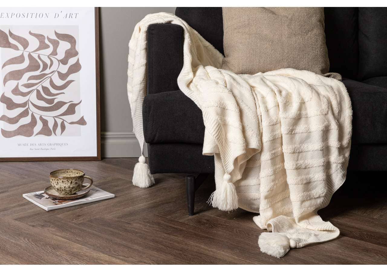 Ljust, lyxigt pläd i ull på mörk soffa för mysig heminredning och komfort.