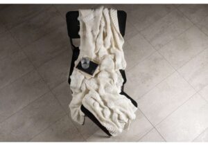 Mjukt shetternett täcke på svart stol, med glas, bok och anteckningsbok i beige nyanser.