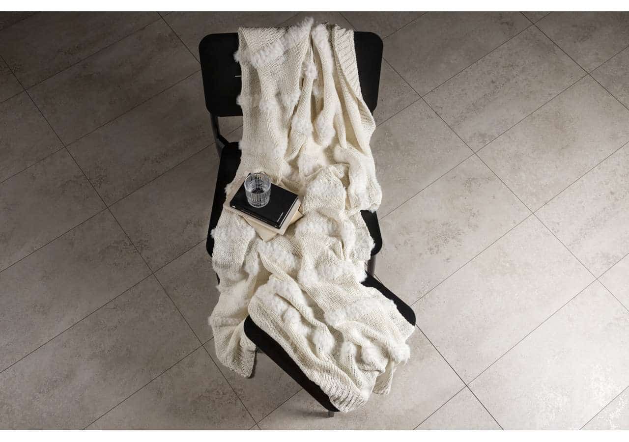 Mjukt shetternett täcke på svart stol, med glas, bok och anteckningsbok i beige nyanser.