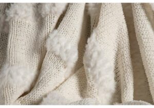 Ljus cremefärgad stickad filt med fluffiga kanter, perfekt för säng och heminredning.