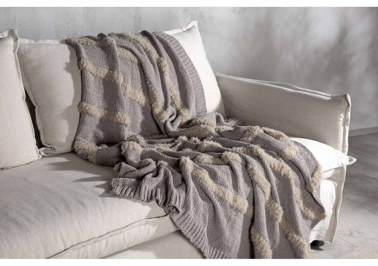 Mysig ullfilt på vit soffa med kuddar, stilfull och varm inredningsdetalj.