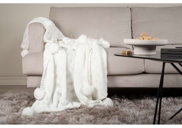 Mjuk vit ullfilt på beige soffakudde i vardagsrum.