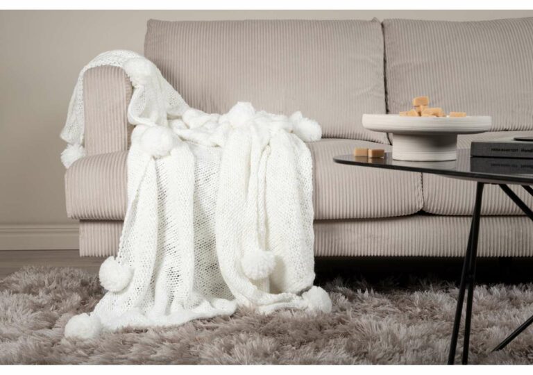 Mjuk vit ullfilt på beige soffakudde i vardagsrum.