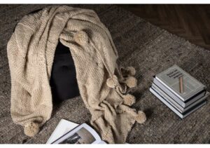 Mjukt stickat filttäcke med pom-pomdetaljer på en antik träsoffa.