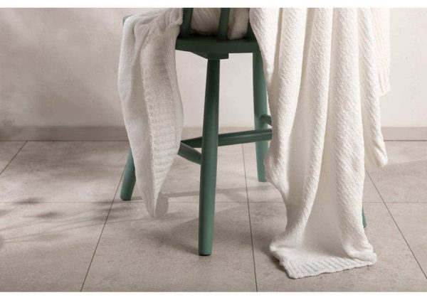 Ljusgrön stol med vit handduk i ett minimalistiskt rum.