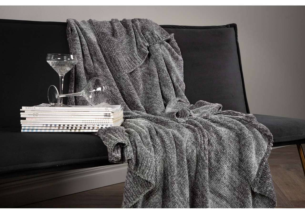 Ljusgrå, mjuk och varm filt på svart soffa med glass och magasin.
