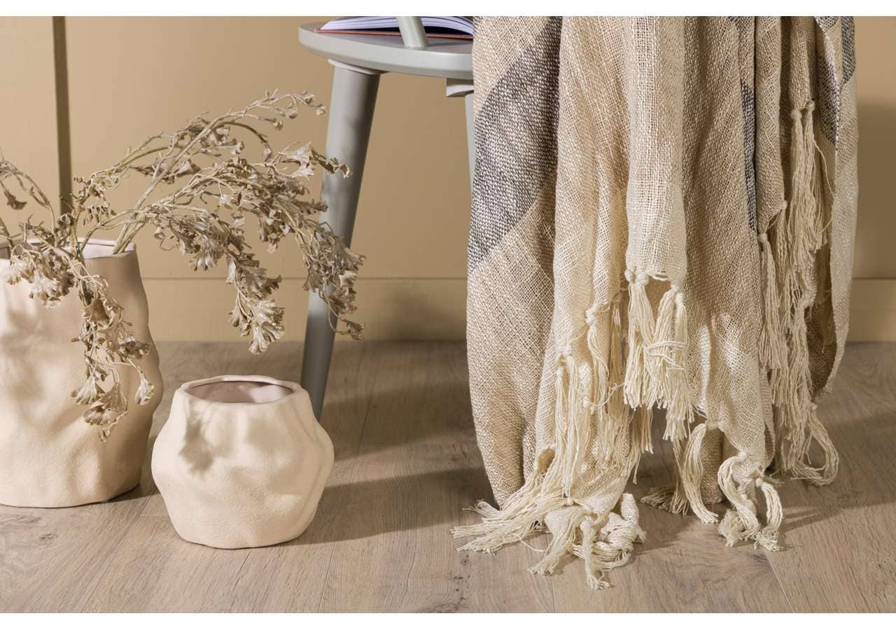 Ljus, naturfärgade vaser med torra blommor och textilfiltret med fransar i beige.