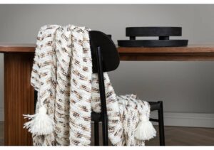 Mysig filt i vitt och brunt på svart stol vid träbord.