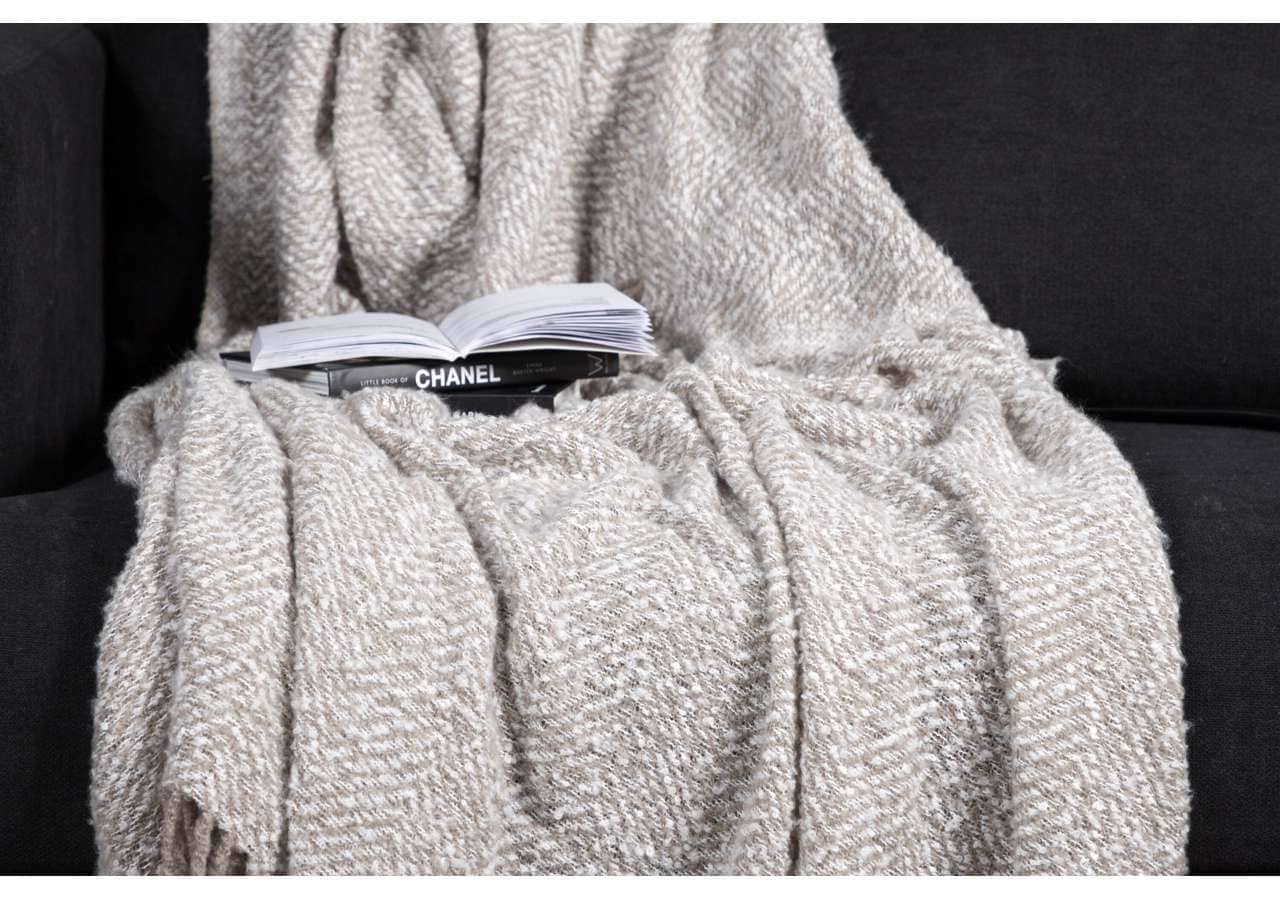 Mjukt beige makramé filt eller throw på svart soffa, perfekt för mys och avkoppling.