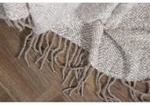 Nyanserad, mjuk och stilren textilbild av en handvävd matta med långa fransar på trägolv.