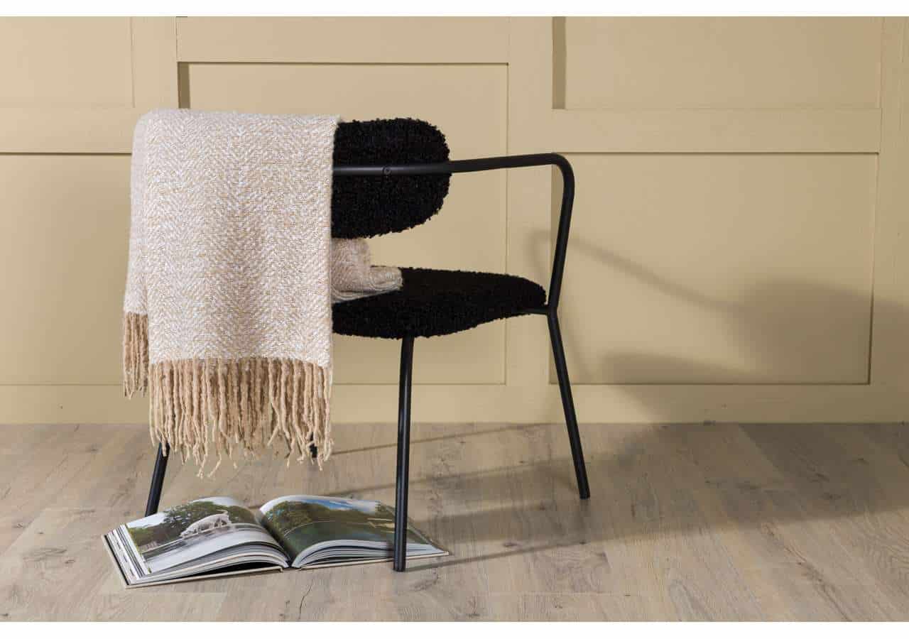 Mjuk ullfilt på svart stol mot beige vägg, perfekt till sovrum eller vardagsrum.