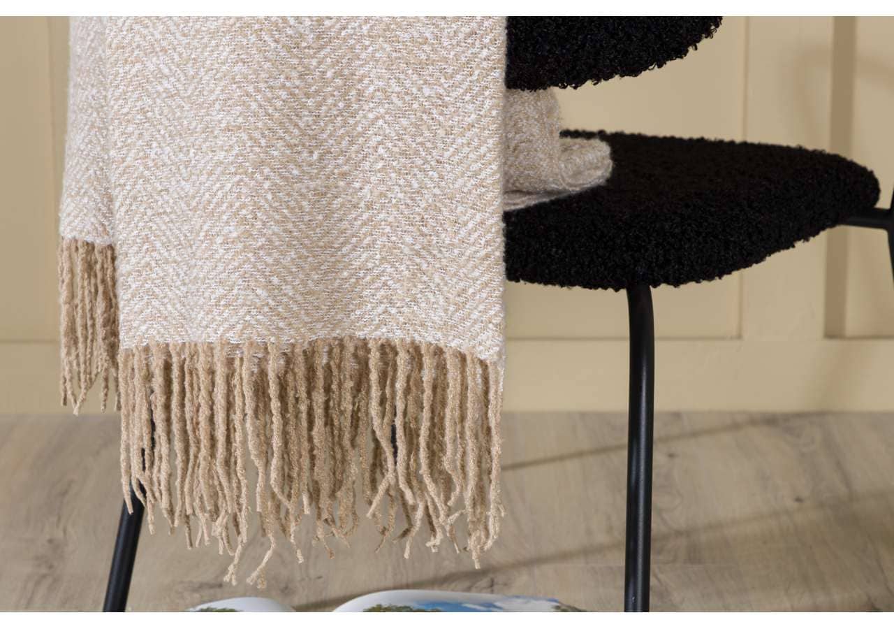 Mjuk filt i naturfärger hänger på stol, perfekt för mysiga hem.