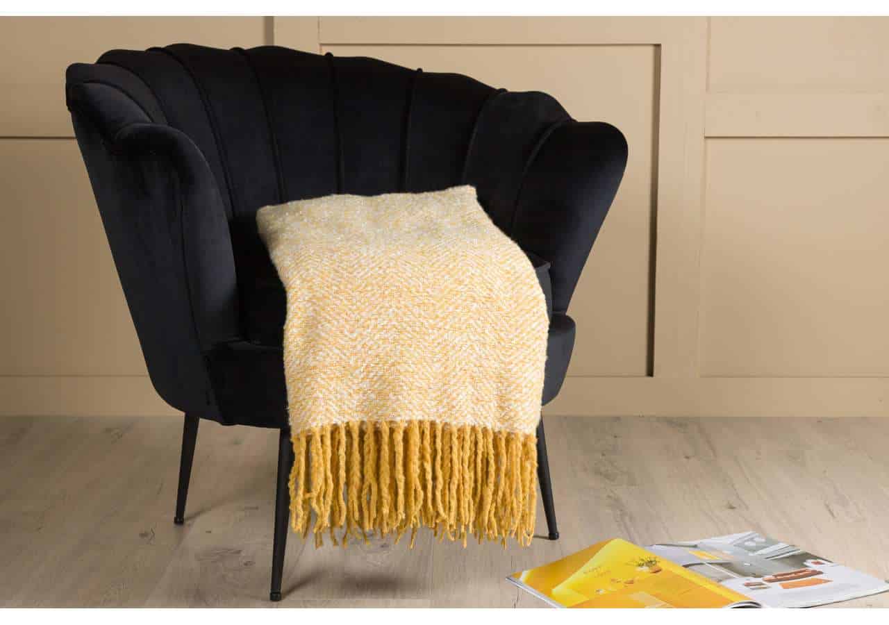 Mjukt gul- och vitrandigt afghan på svart fåtölj, mysig inredningsdetalj från Sängfabriken.