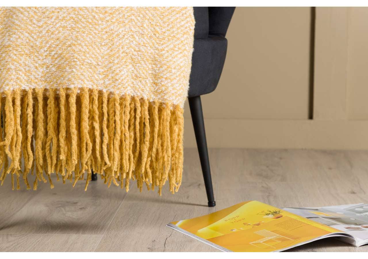 Varm gulstickad filt med tasselavslutning, stilren och mysig för hemmet.
