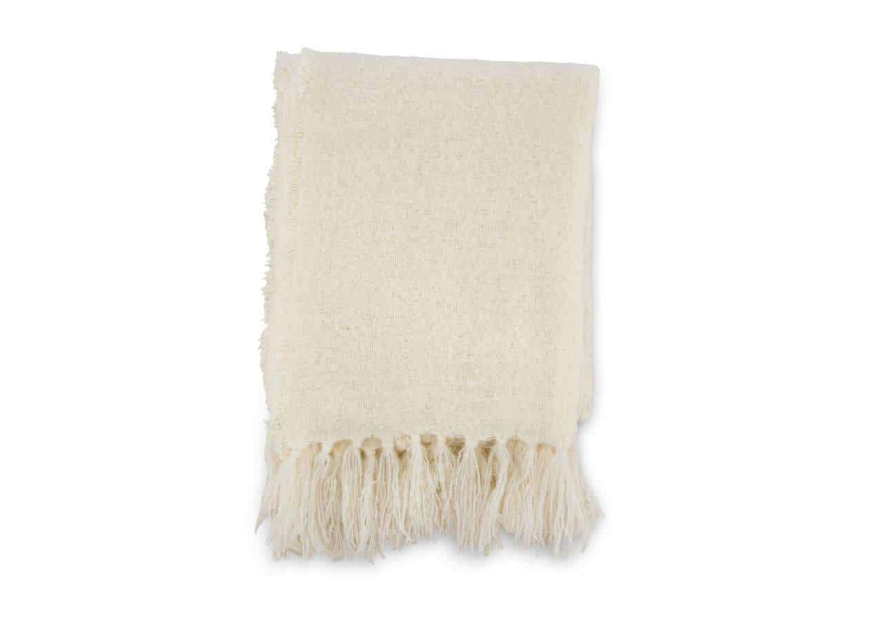 Ljus krämfärgad ullpläd med fransar, perfekt för sängkläder eller avkoppling.