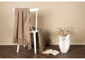 Mysig filt i beige på stol med öppen bok och blomster vas, bohemisk inredning, känsla av stil och komfort.