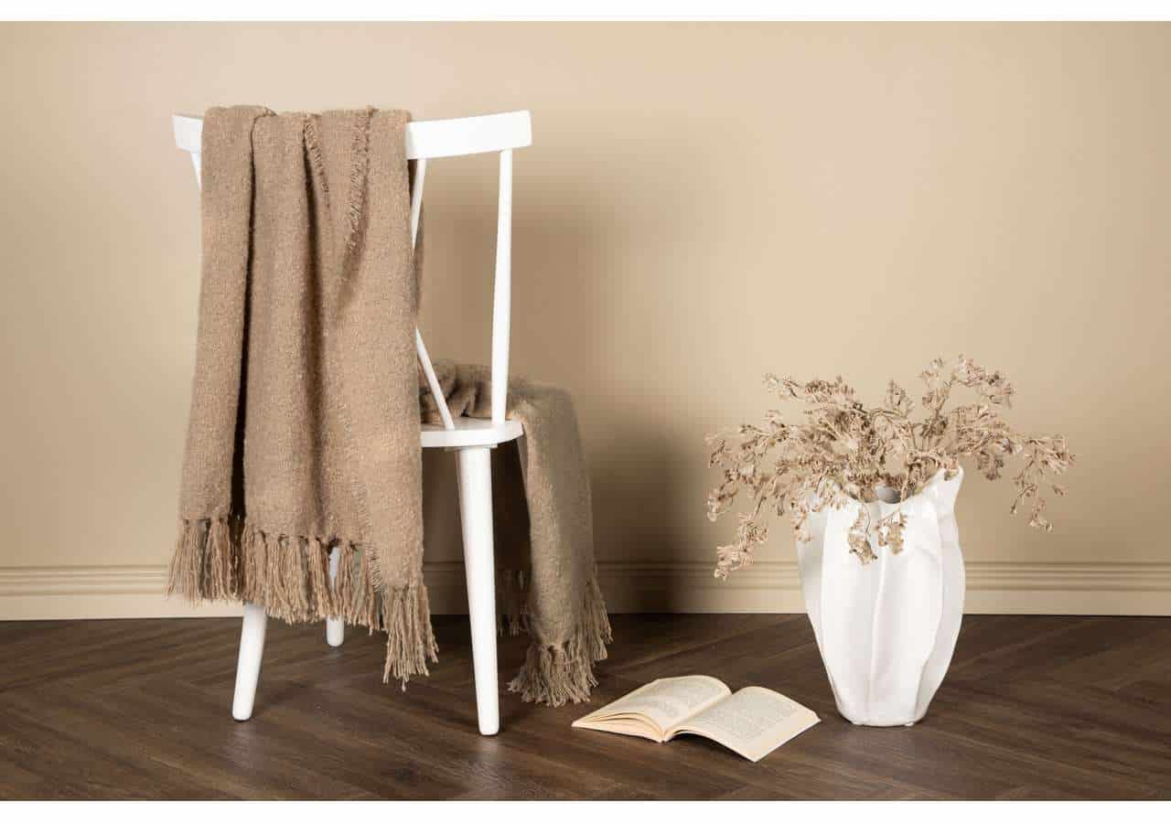 Mysig filt i beige på stol med öppen bok och blomster vas, bohemisk inredning, känsla av stil och komfort.