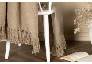Ljusbrun mysig pläd på vit stol med trähörn, perfekt för sovrum eller vardagsrum.