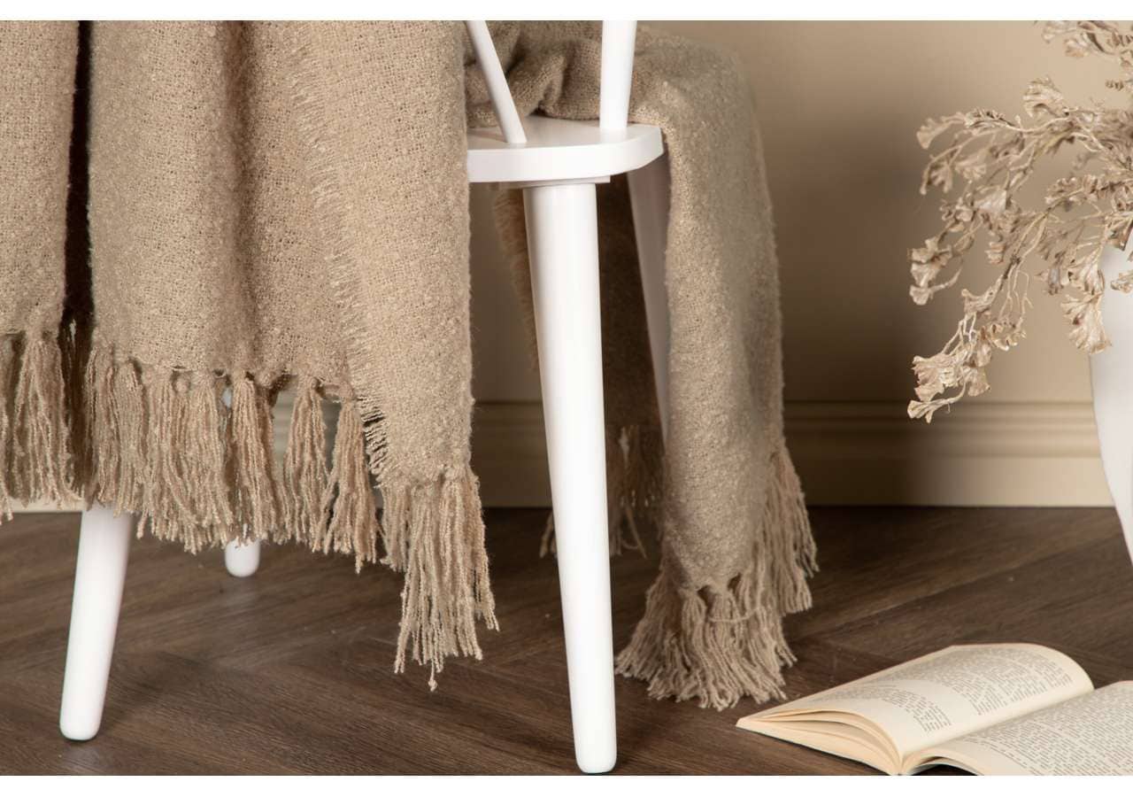 Ljusbrun mysig pläd på vit stol med trähörn, perfekt för sovrum eller vardagsrum.