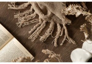 Ullhalsduk i naturfärger på träbord med bok och vaser.