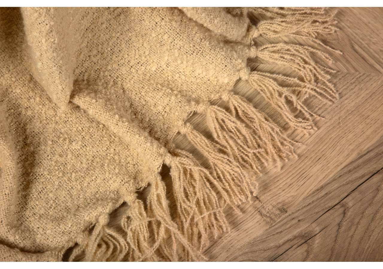 Mjukt ullpläd med långa fransar på träbaksida.