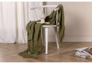 Mjuk grön pläd på vit trästol i ett elegant sovrums/interiör.