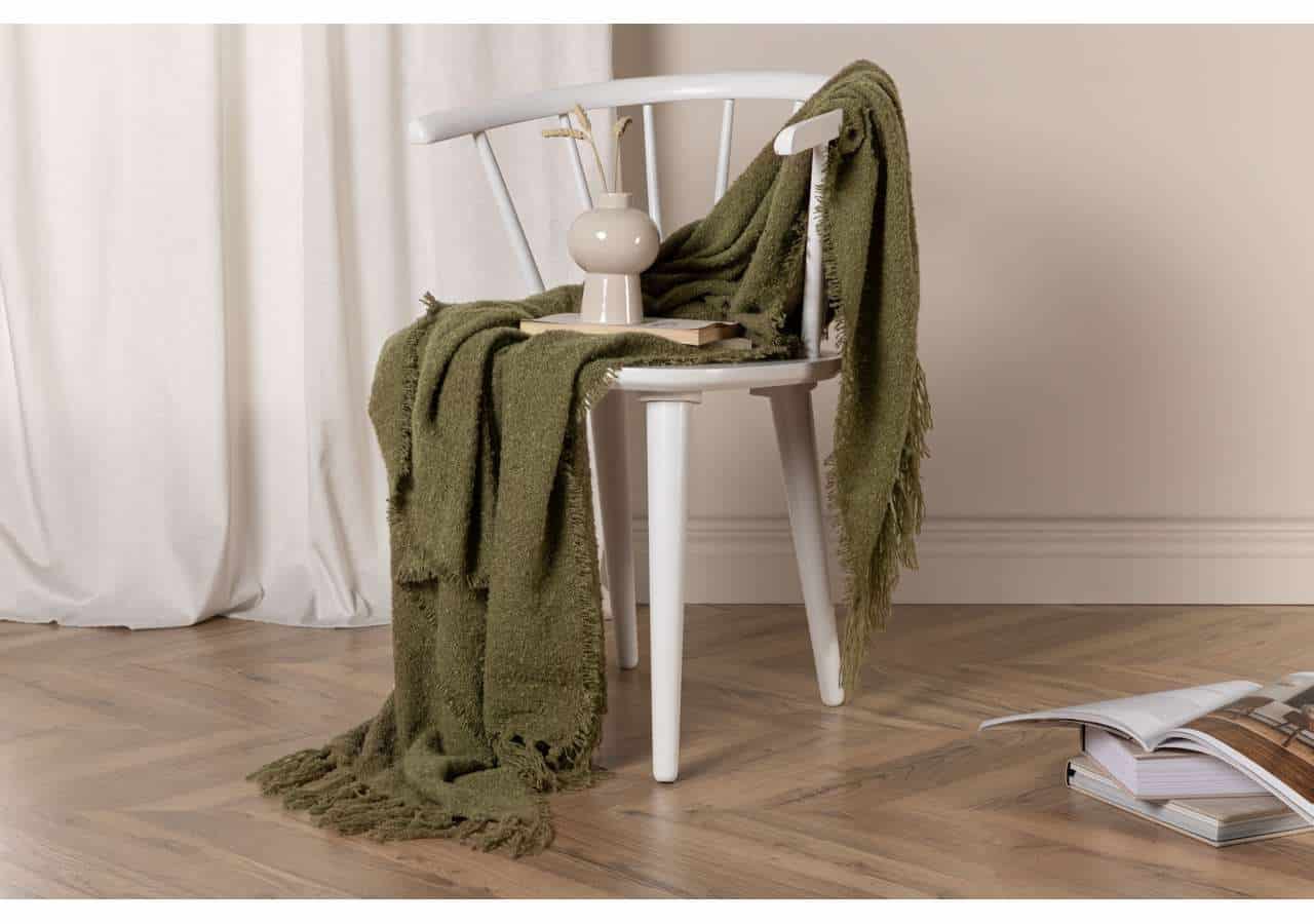 Mjuk grön pläd på vit trästol i ett elegant sovrums/interiör.