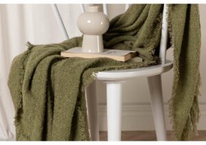 Mjuk grön gosseydda filt på vit trästol för skön sömn och komfort.