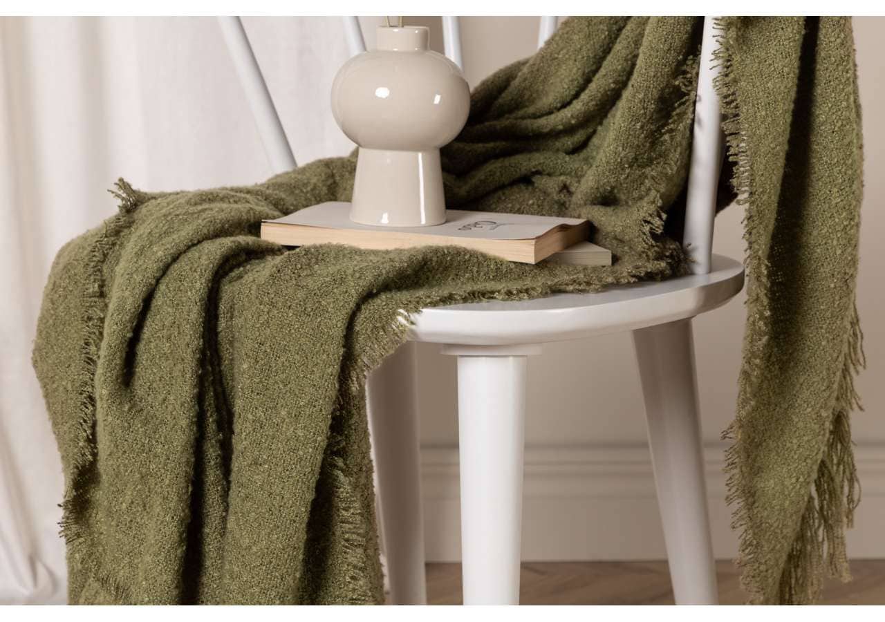 Mjuk grön gosseydda filt på vit trästol för skön sömn och komfort.